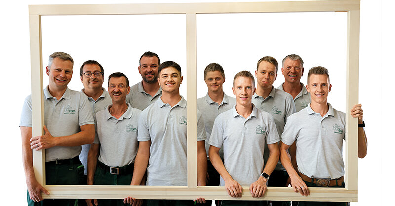 Team in grauen Shirts hält einen Holzrahmen und guckt durch