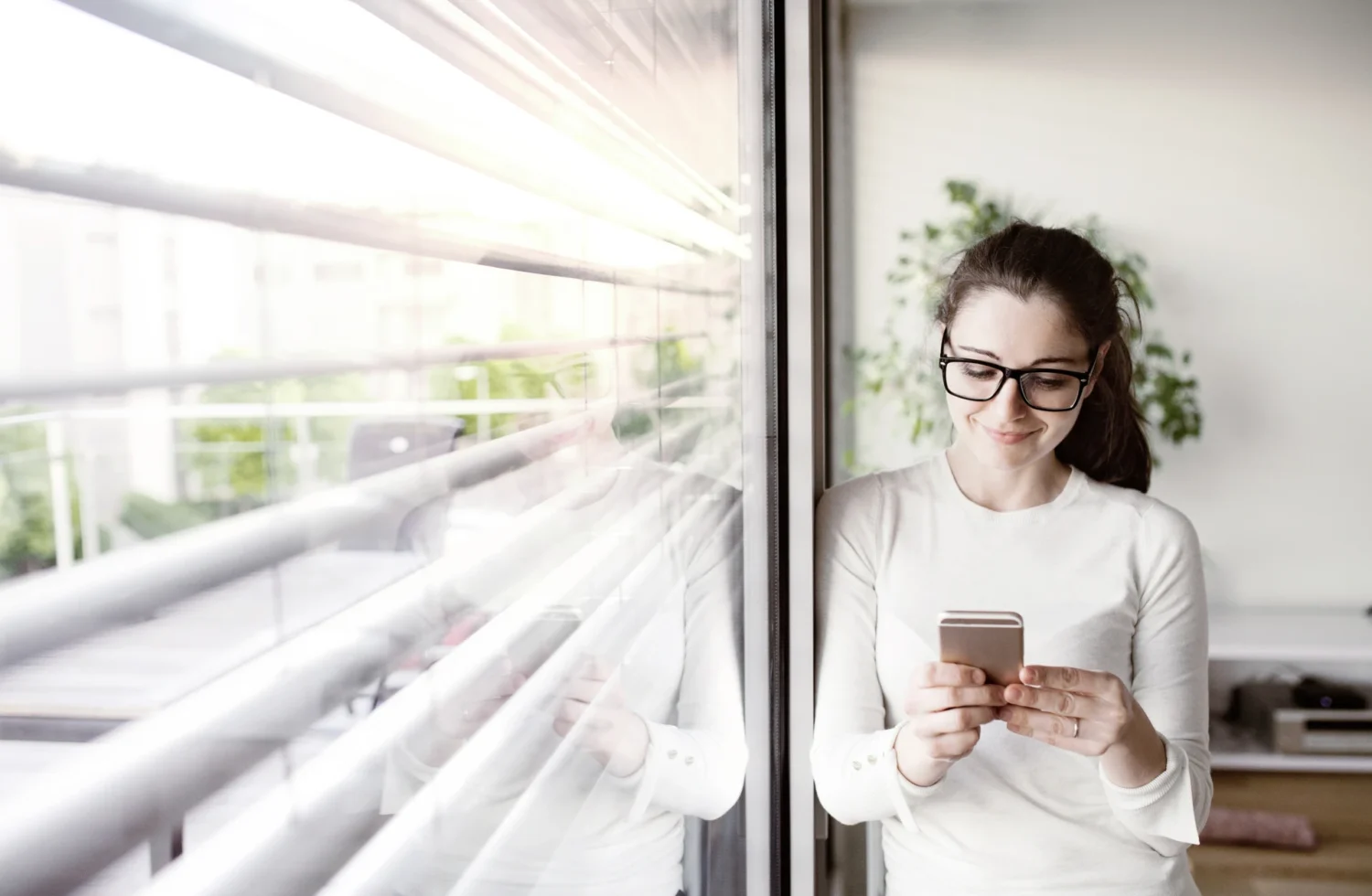 Frau steht mit Smartphone am Fenster