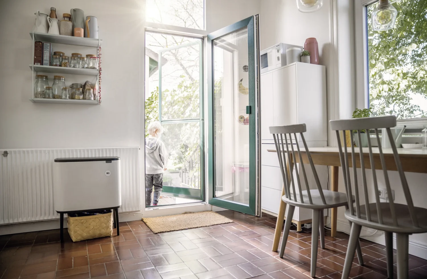 Kind steht in einer hellen Küche neben einer geöffneten Terrassentür